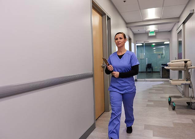 Nurse holding clipboard and walking down hospital hallway