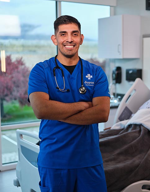 Joyce nursing student in blue uniform standing in our nursing simulation lab