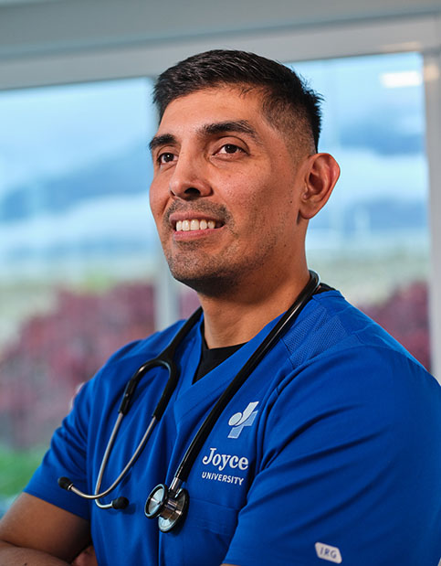 Joyce nursing student wearing blue scrubs and stethoscope smiling with arms crossed
