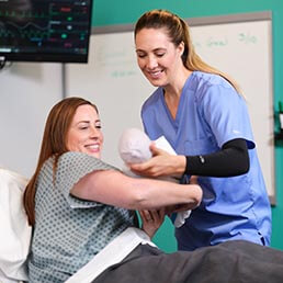 Nurse handing newborn to mother in maternity ward of a hospital