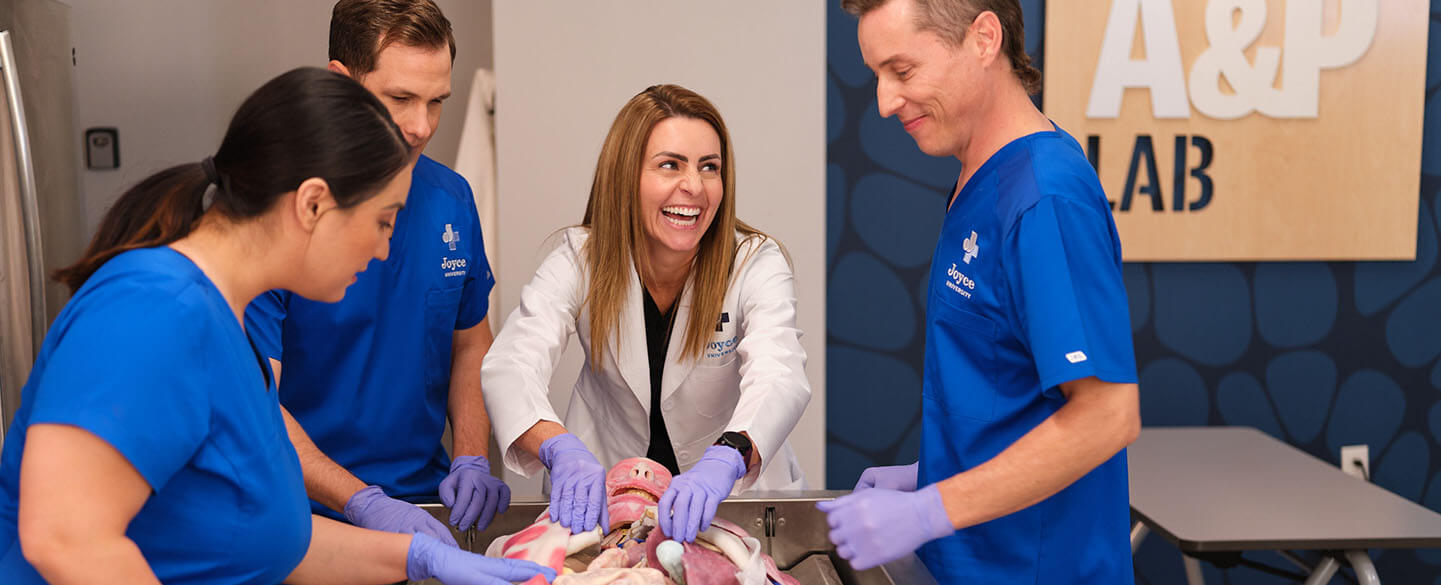 Joyce University faculty teach three students in blue scrubs on synthetic cadaver in Joyce Johnson simulation center