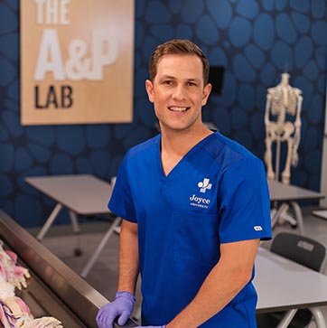 Joyce University student in blue scrubs smiling and standing in the anatomy and physiology lab