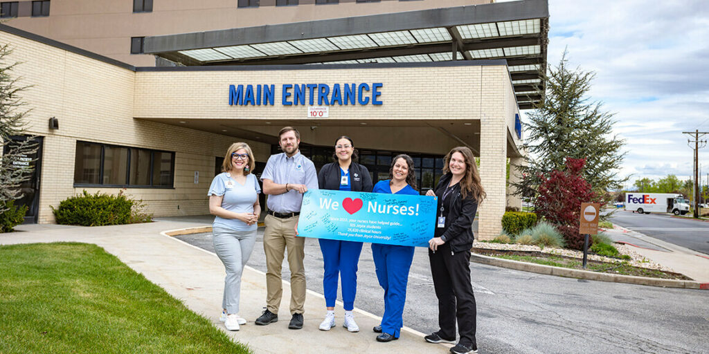 joyce university staff giving hospital nursing staff a giant blue thank you card with we heart nurses on it