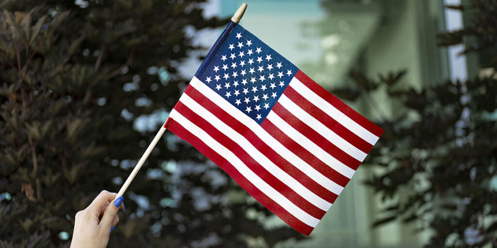 woman holding a small american flag in front of the Joyce University campus