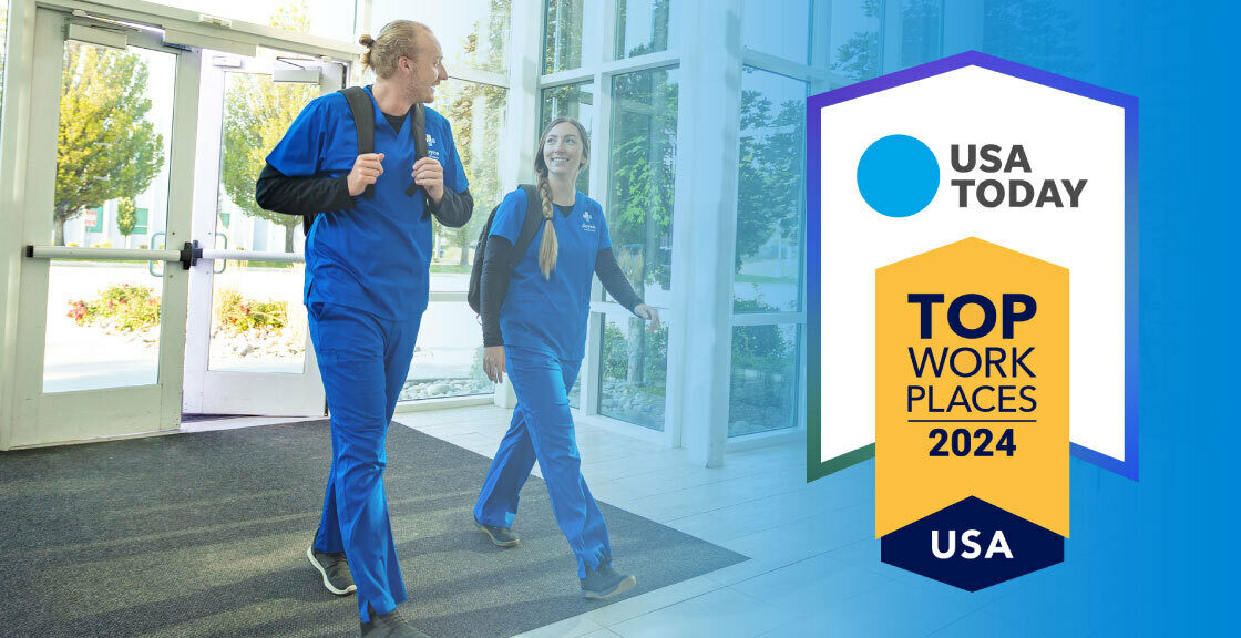 Two Joyce University students in blue scrubs walking through the vestibule. Graphic overlay of the USA Today Logo and the text Top Workplaces 2024