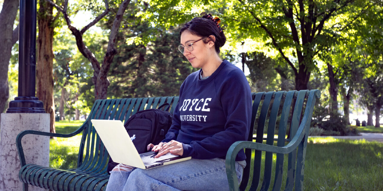 Joyce University student sitting on a park bench with their laptop