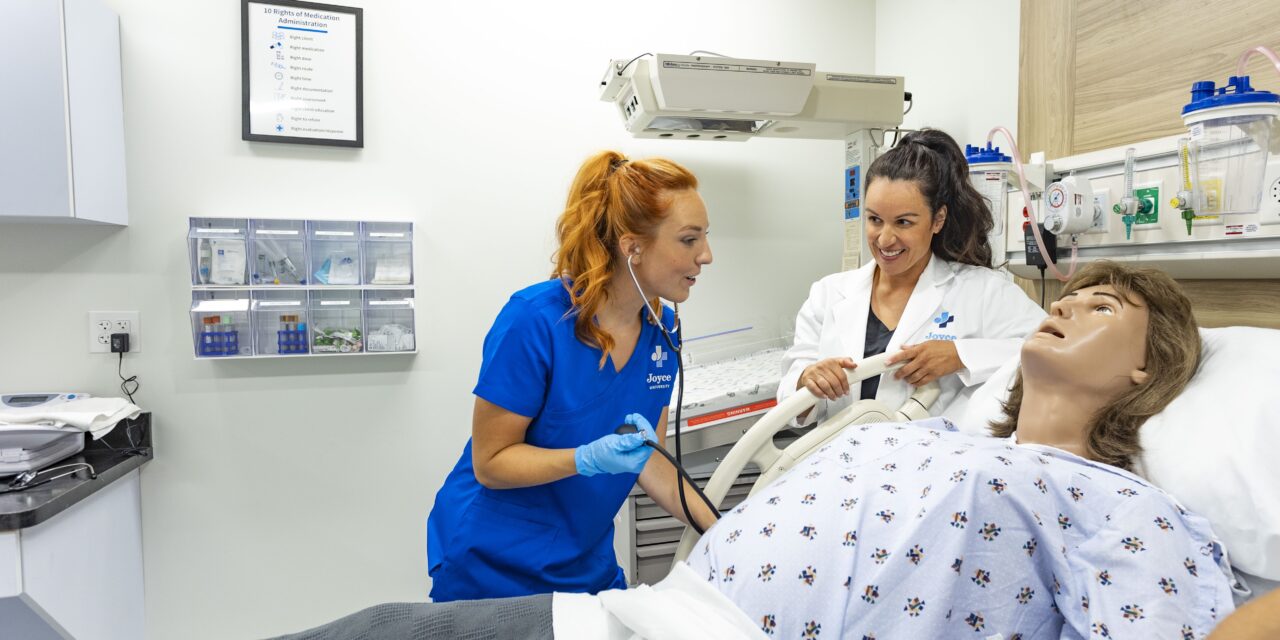 joyce nursing student taking pulse on high-fidelity learning mannequin under direction of simulation instructor