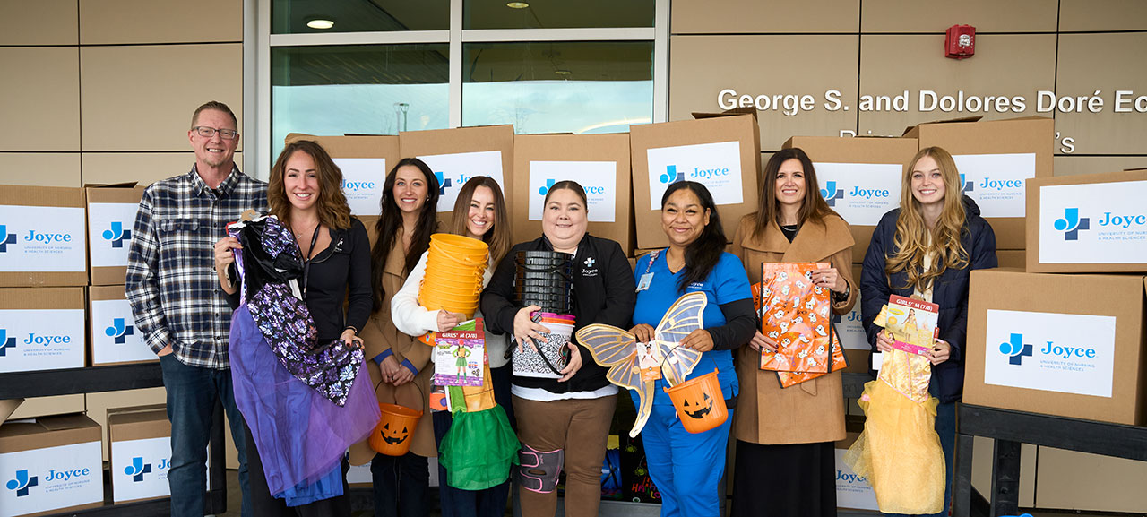 joyce university staff holding halloween costumes outside of primary childrens hospital during charity costume drive.