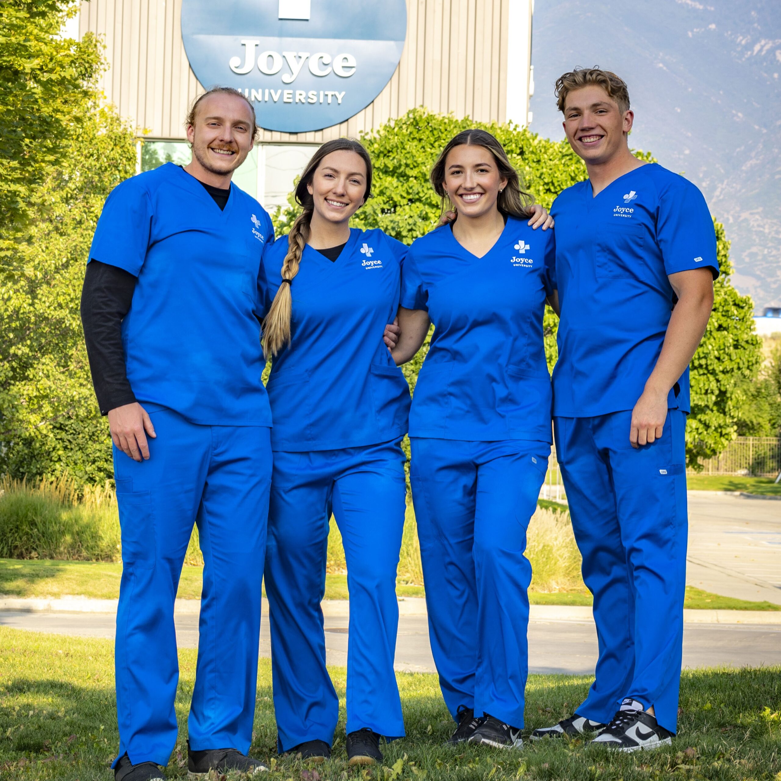 four joyce university alumni standing in front of campus building